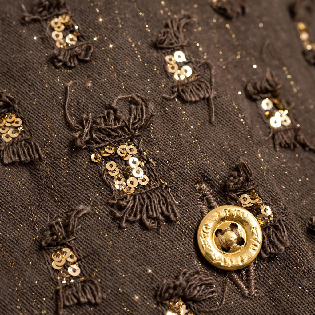 Detalle de chaqueta las cucadas de erisa marrón con lentejuelas doradas, hilos deshilachados y botón metálico dorado.