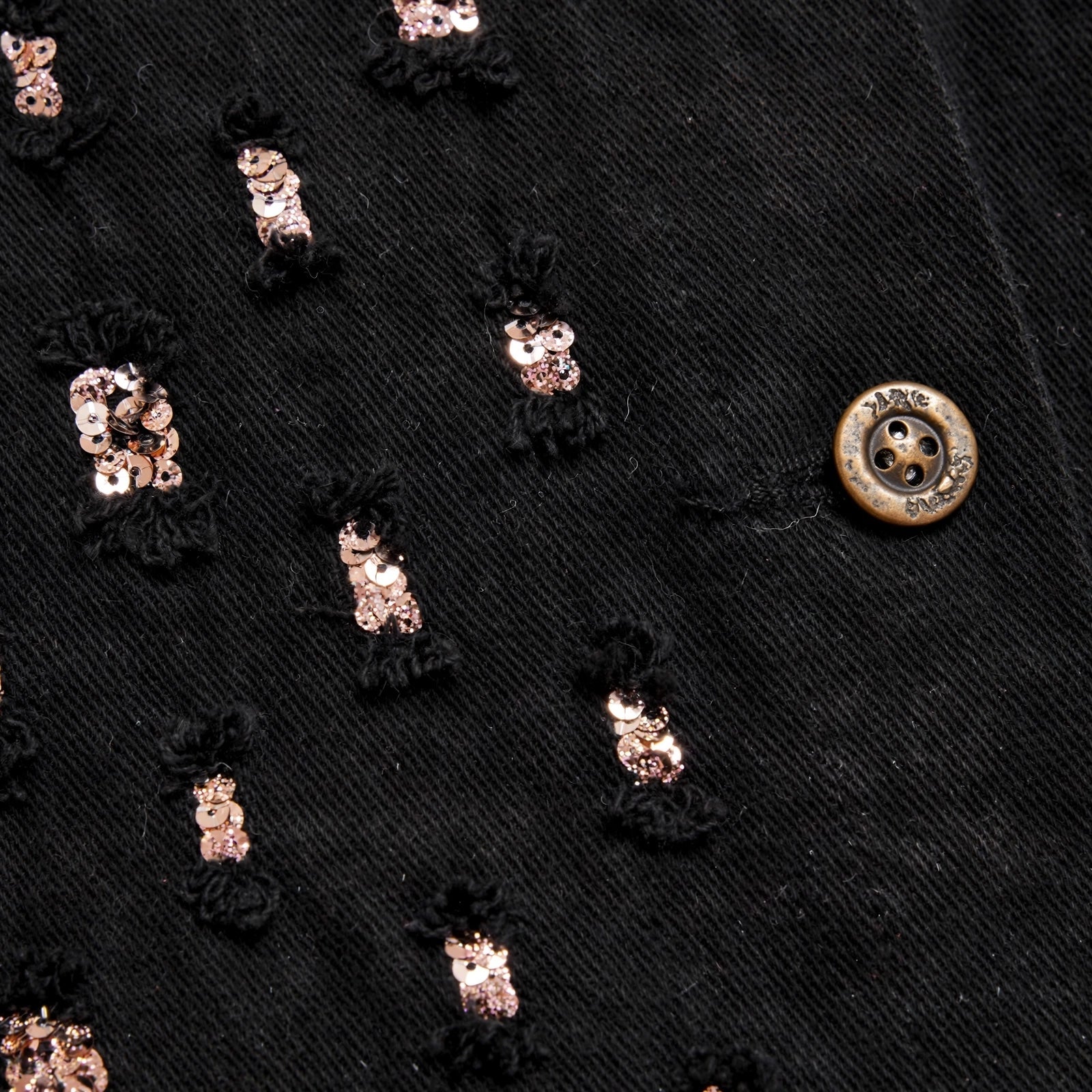 Detalle de chaqueta de mezclilla negra las cucadas de erisa con lentejuelas metálicas y botón grabado
