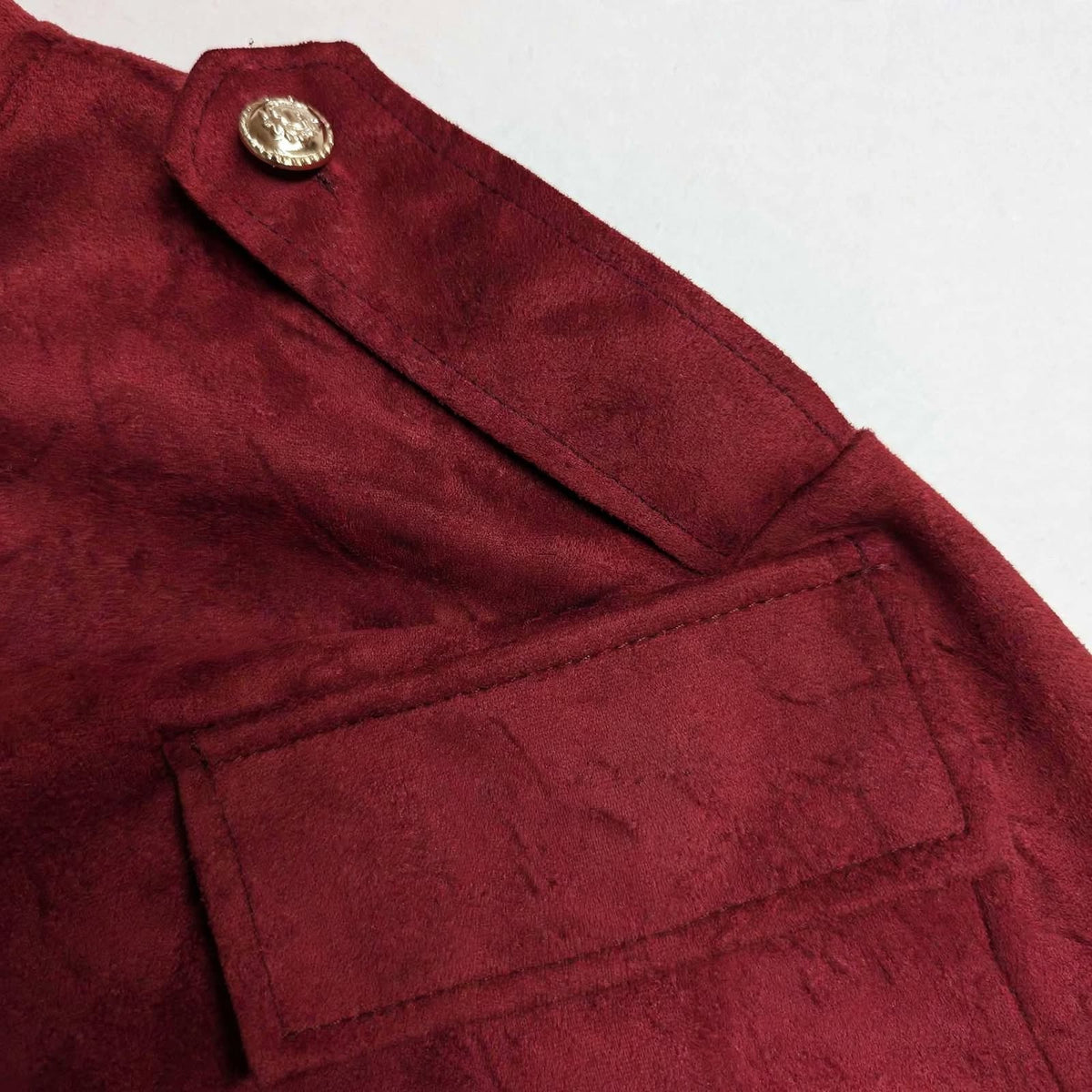 Detalle de chaqueta las cucadas de erisa en color burdeos, tejido efecto ante con botón dorado y bolsillo con solapa.