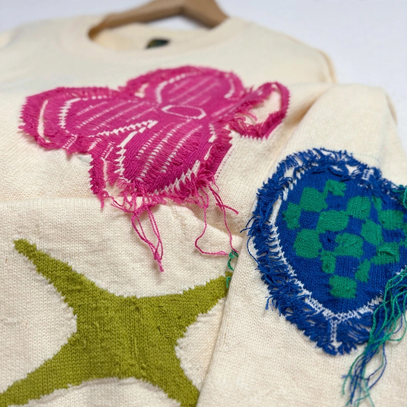 Jersey de punto crema de las cucadas de erisa con bordados vibrantes fucsia, verde y azul y detalles deshilachados.