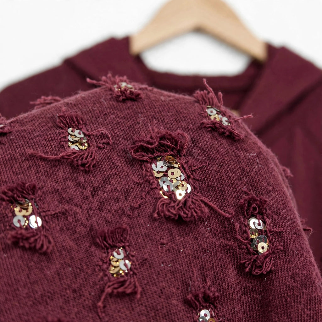 Detalle de sudadera burdeos las cucadas de erisa con lentejuelas brillantes y textura deshilachada en tejido suave