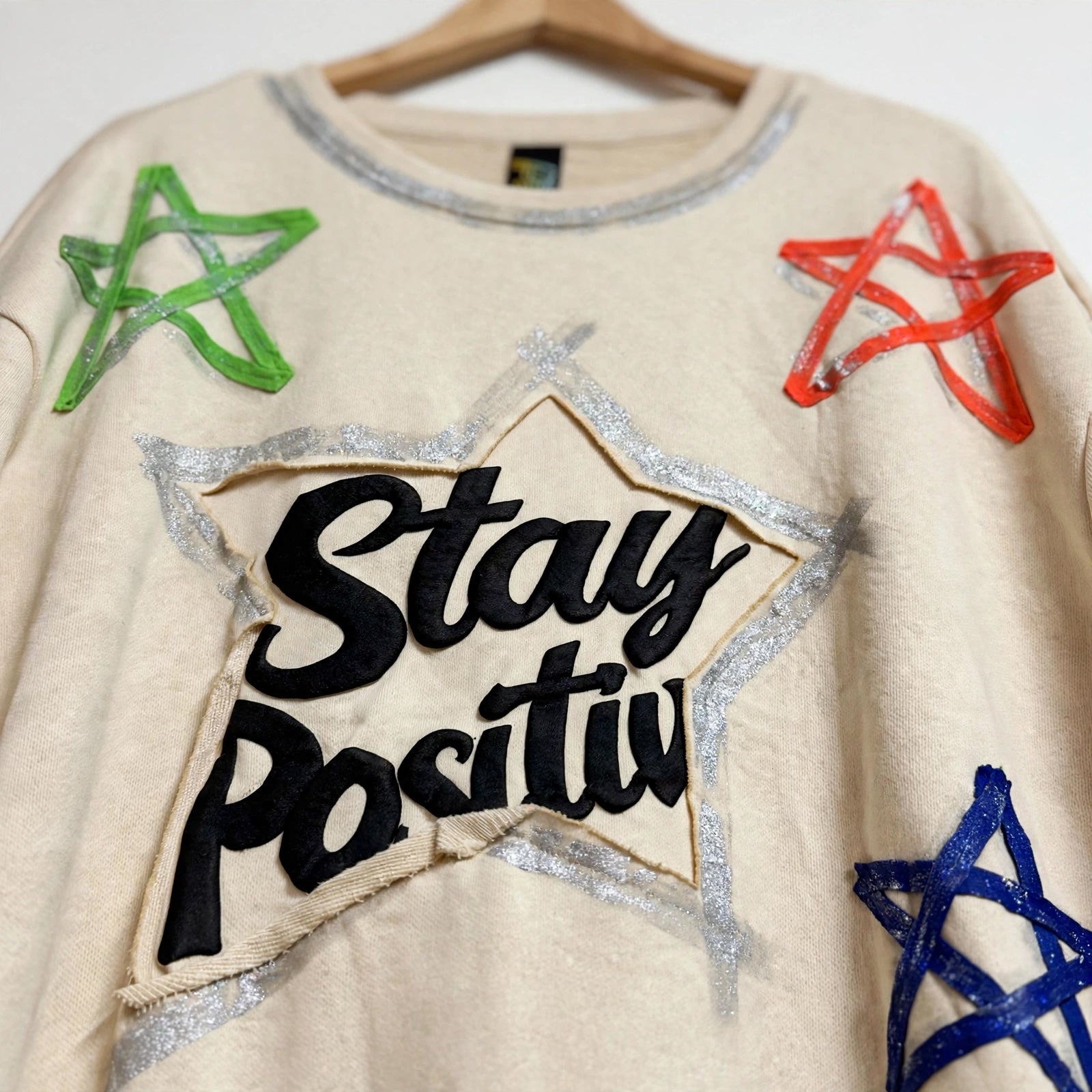 Sudadera las cucadas de erisa color crema con estrellas de colores, glitter plateado y bordado Stay Positive