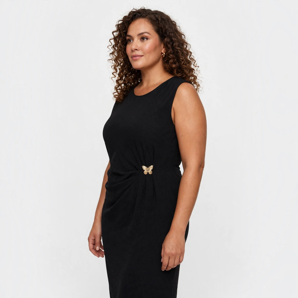 Modelo con vestido midi negro sin mangas de las cucadas de erisa, con detalle de broche de mariposa y cintura fruncida.