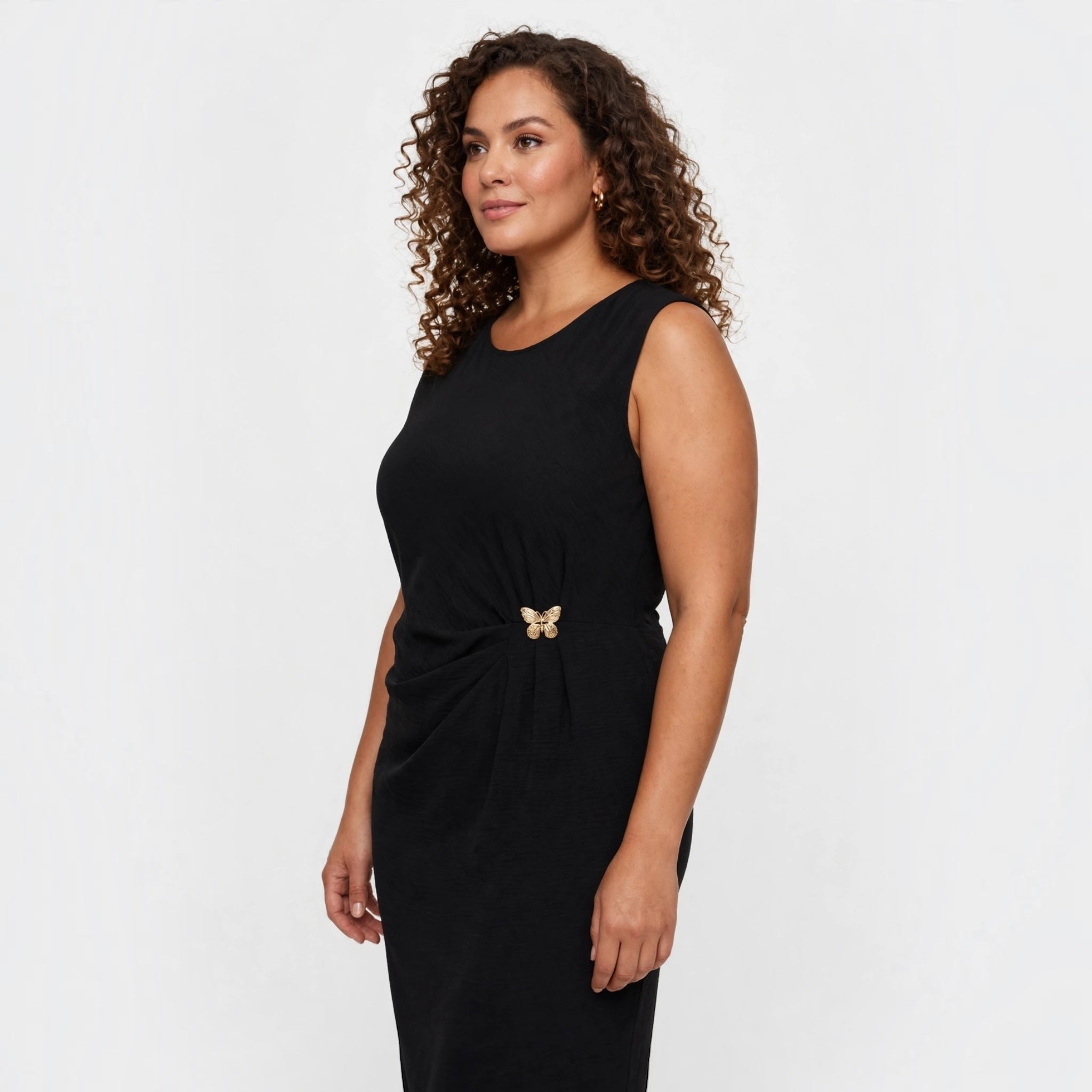 Modelo con vestido midi negro sin mangas de las cucadas de erisa, con detalle de broche de mariposa y cintura fruncida.